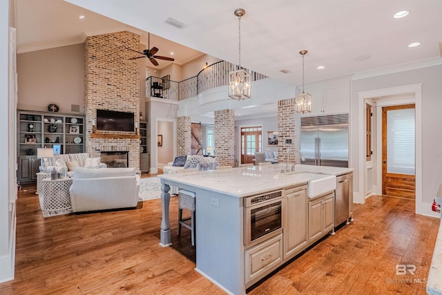 kitchen with decorative light fixtures, light hardwood / wood-style floors, a large island with sink, and appliances with stainless steel finishes