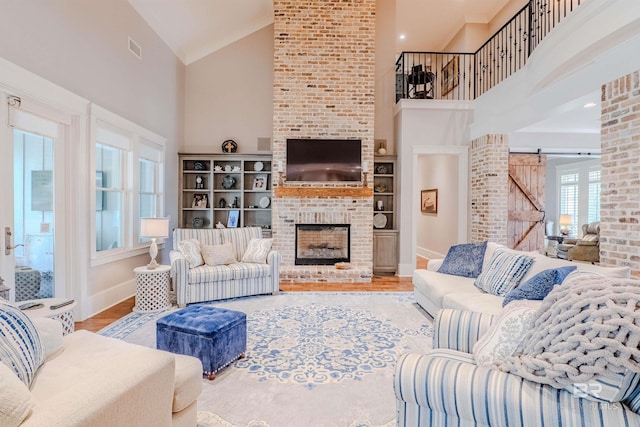 living room featuring hardwood / wood-style floors, a fireplace, high vaulted ceiling, and a barn door