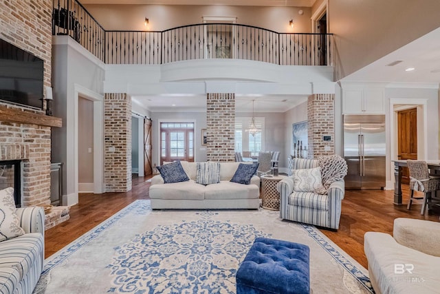 living room featuring crown molding, a towering ceiling, a fireplace, wood-type flooring, and ornate columns