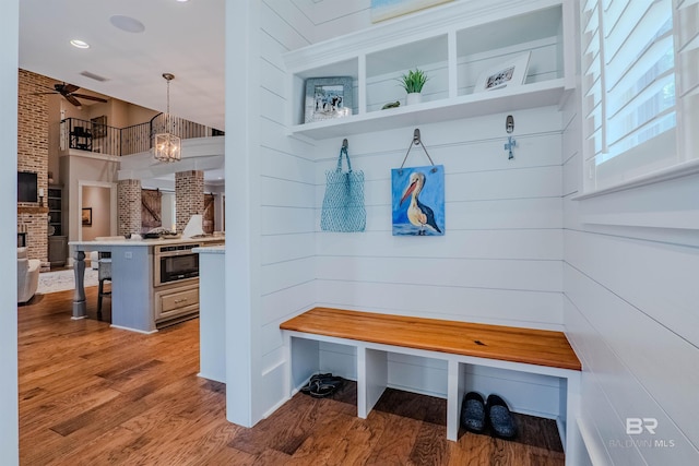 mudroom featuring ceiling fan with notable chandelier, a fireplace, light hardwood / wood-style floors, and brick wall