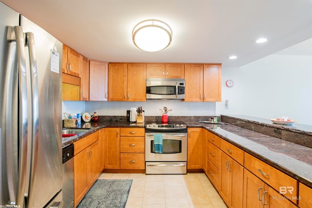 kitchen with dark stone countertops, sink, light tile patterned floors, and appliances with stainless steel finishes