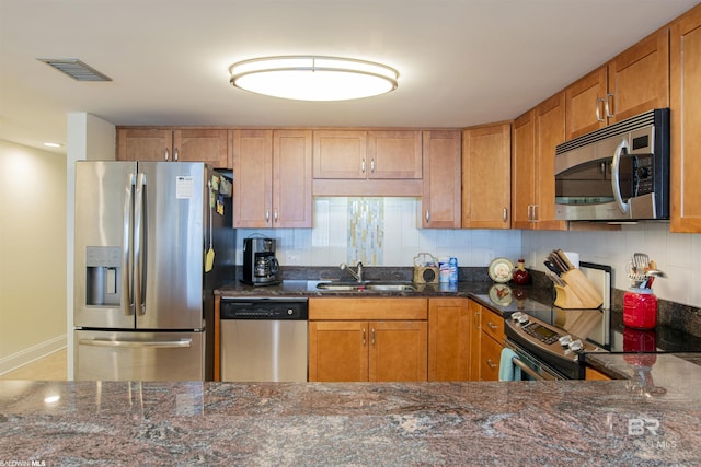 kitchen featuring visible vents, dark stone counters, a sink, appliances with stainless steel finishes, and backsplash