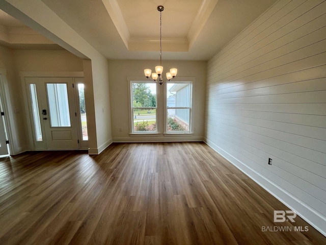 unfurnished dining area with an inviting chandelier, a raised ceiling, dark wood-type flooring, and wood walls