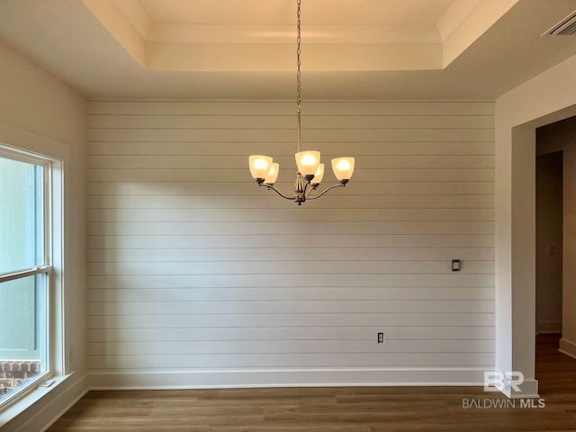 unfurnished dining area featuring a tray ceiling, an inviting chandelier, a wealth of natural light, and dark wood-type flooring