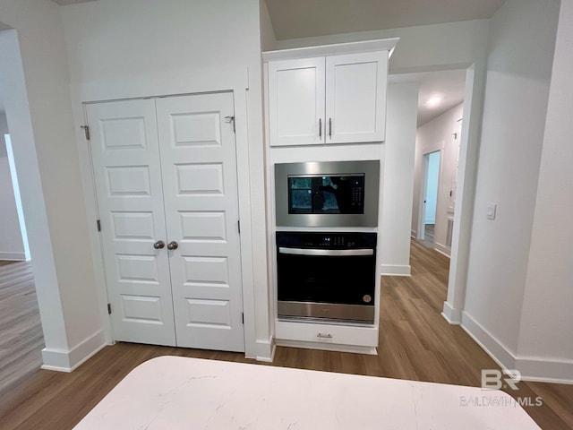 kitchen featuring built in microwave, stainless steel oven, white cabinets, and hardwood / wood-style floors