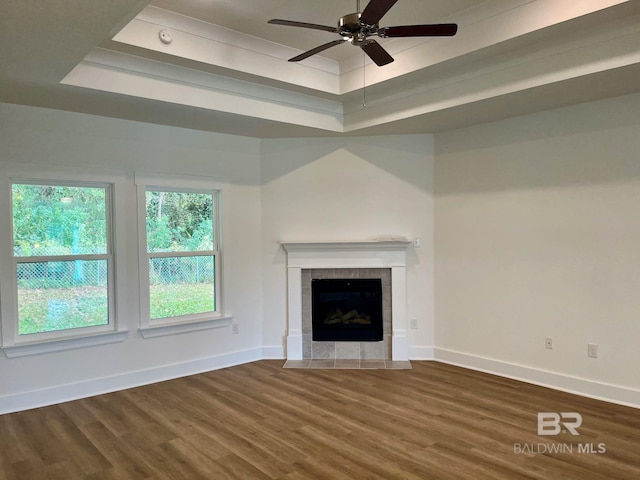 unfurnished living room featuring ceiling fan, dark hardwood / wood-style flooring, a raised ceiling, and a tile fireplace