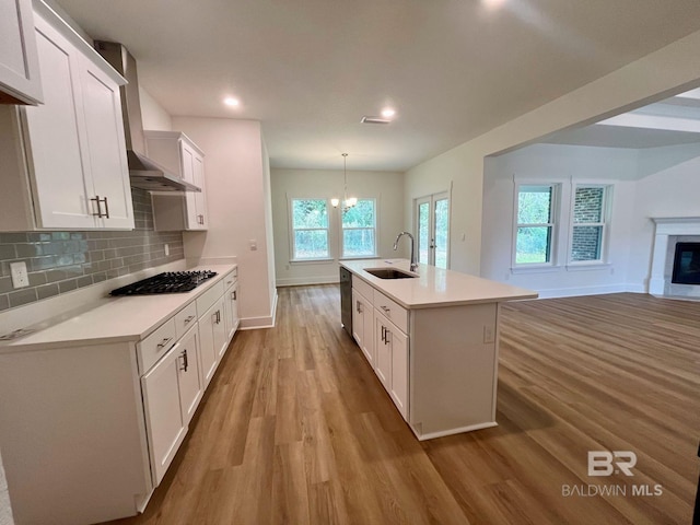 kitchen featuring white cabinetry, sink, stainless steel appliances, decorative light fixtures, and a center island with sink