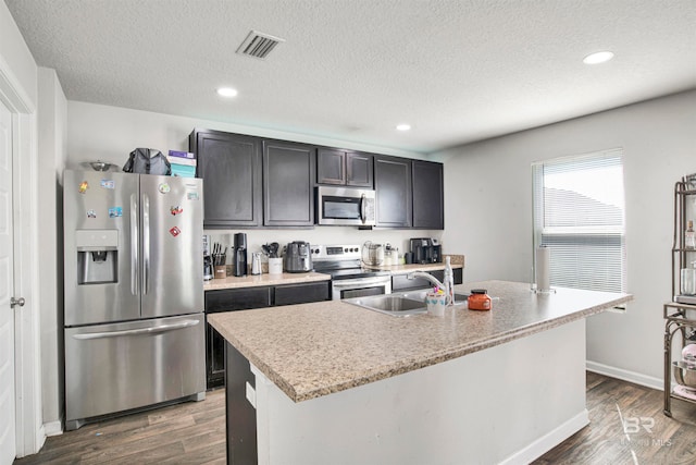 kitchen with appliances with stainless steel finishes, an island with sink, sink, and dark wood-type flooring