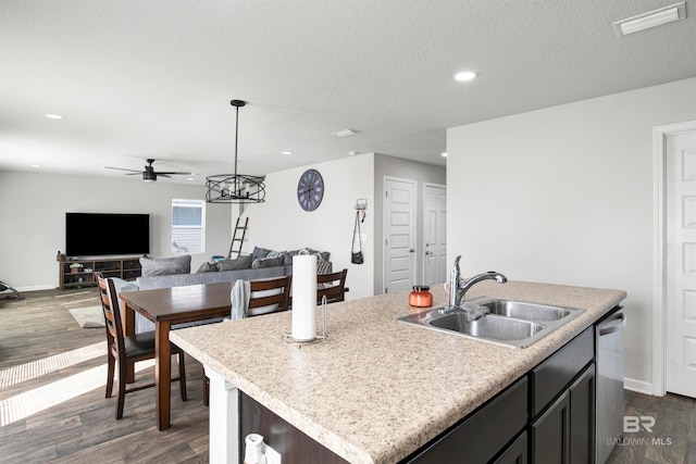 kitchen with a textured ceiling, dishwasher, sink, dark wood-type flooring, and a center island with sink