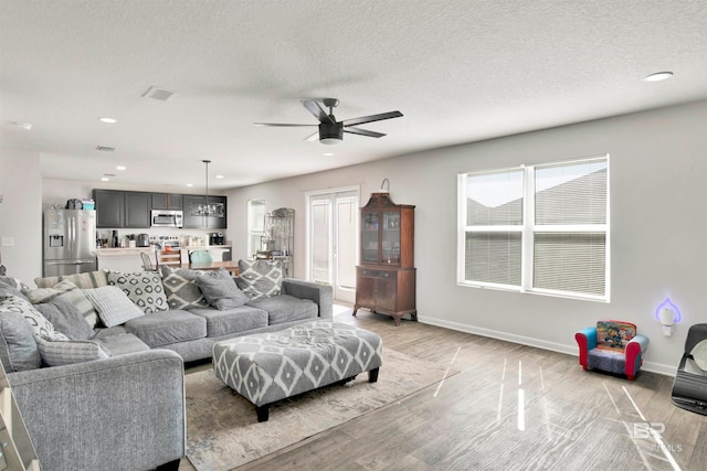 living room with a textured ceiling, ceiling fan, and light wood-type flooring