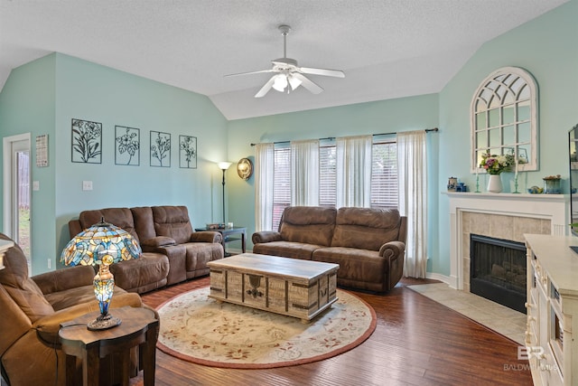 living area with lofted ceiling, ceiling fan, a textured ceiling, a fireplace, and wood finished floors