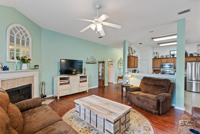 living area featuring ceiling fan, lofted ceiling, visible vents, dark wood-style floors, and a tiled fireplace