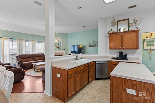 kitchen with brown cabinetry, open floor plan, a sink, and stainless steel dishwasher