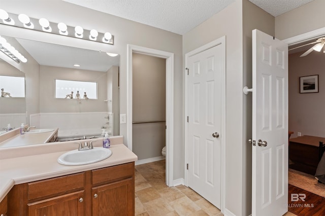 full bath with baseboards, toilet, ceiling fan, a textured ceiling, and vanity