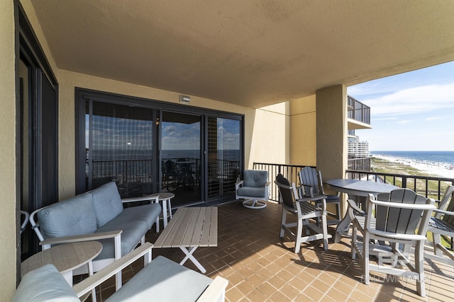 balcony with an outdoor hangout area, a water view, and a view of the beach