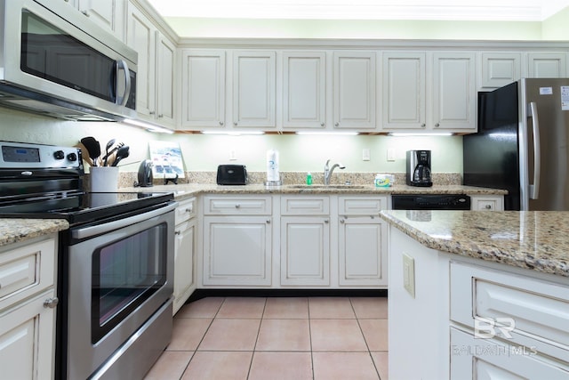 kitchen featuring light tile patterned floors, light stone countertops, stainless steel appliances, white cabinetry, and a sink