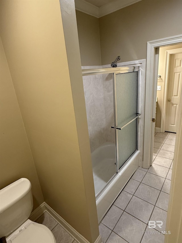 full bathroom featuring toilet, baseboards, bath / shower combo with glass door, and tile patterned floors