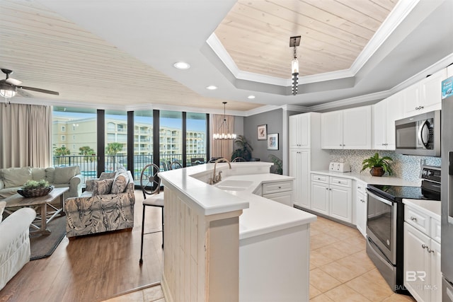 kitchen featuring hanging light fixtures, ceiling fan with notable chandelier, an island with sink, appliances with stainless steel finishes, and backsplash