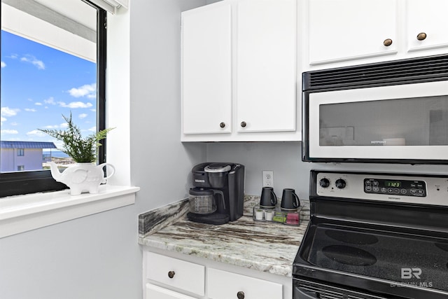 kitchen with light stone countertops, black stove, and white cabinetry