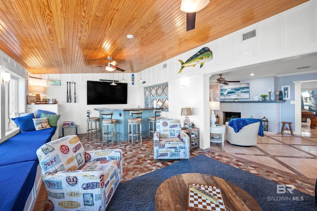 living area with a ceiling fan, a brick fireplace, wood ceiling, and visible vents