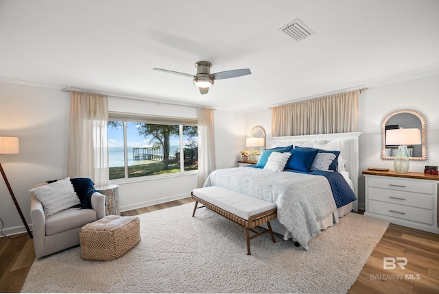 bedroom with ornamental molding, a water view, wood finished floors, and visible vents