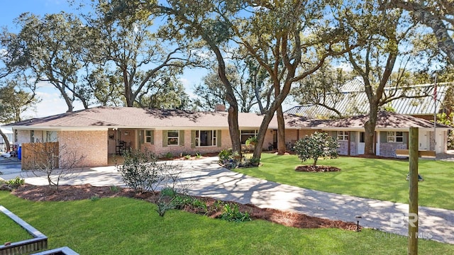 single story home featuring driveway, brick siding, a chimney, and a front yard