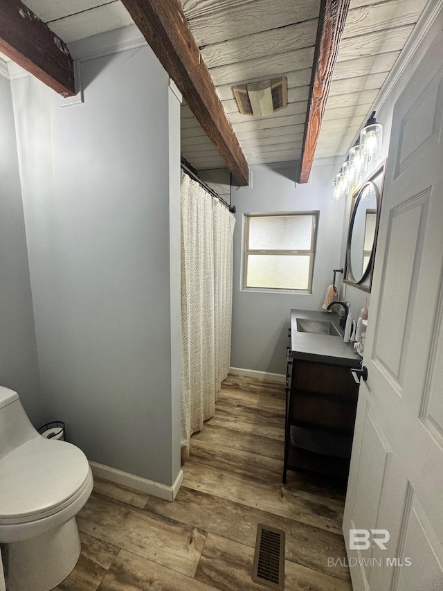 bathroom featuring baseboards, visible vents, toilet, wood finished floors, and beam ceiling