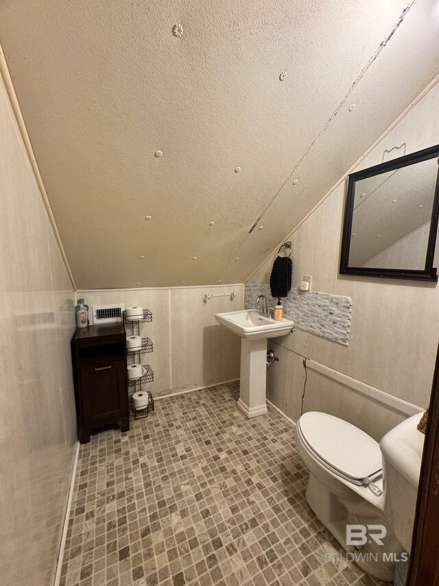 bathroom with toilet, vaulted ceiling, and a textured ceiling