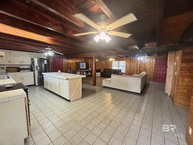 kitchen with tile countertops, wooden walls, stainless steel appliances, and beamed ceiling