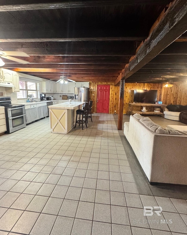 interior space featuring wooden walls, tile countertops, beamed ceiling, stainless steel appliances, and under cabinet range hood