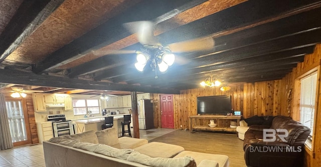 living room with ceiling fan with notable chandelier, wood walls, beam ceiling, and light wood-style floors