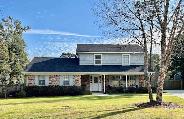 traditional-style house featuring a porch, a front yard, brick siding, and fence