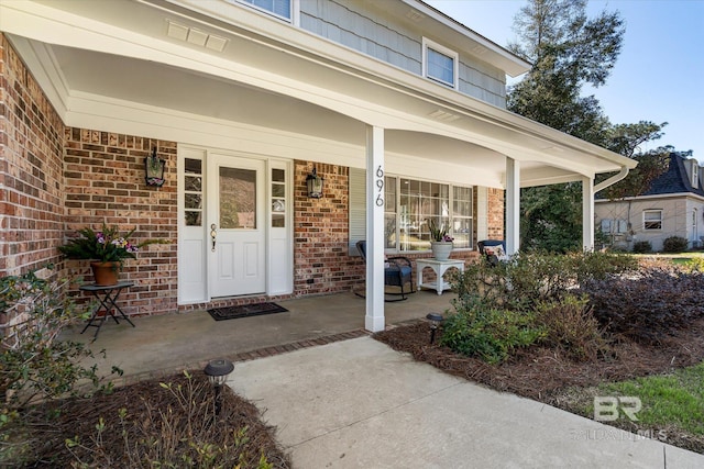 entrance to property featuring covered porch and brick siding