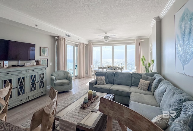 living room featuring a water view, ornamental molding, light hardwood / wood-style floors, and a textured ceiling