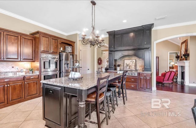 kitchen featuring arched walkways, light stone counters, light tile patterned flooring, stainless steel appliances, and ornamental molding