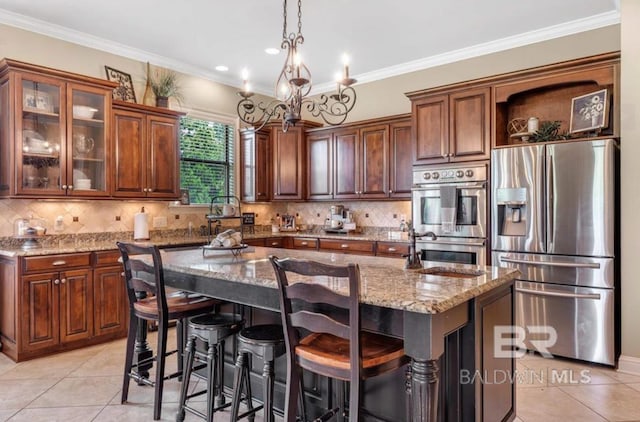 kitchen featuring stainless steel appliances, light stone counters, backsplash, and a center island with sink