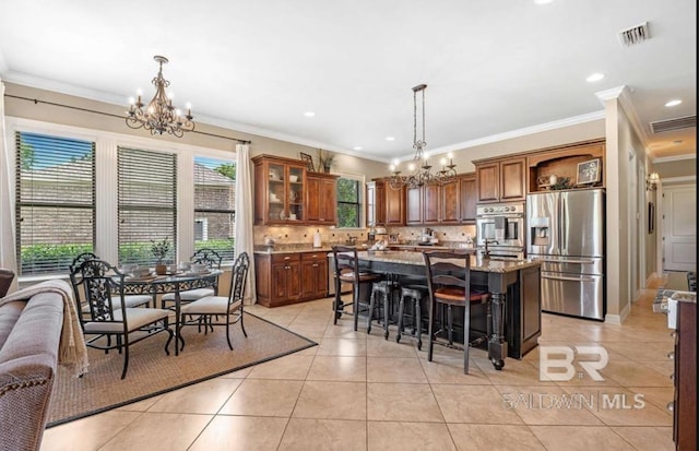 kitchen with light tile patterned floors, a notable chandelier, appliances with stainless steel finishes, backsplash, and a kitchen bar