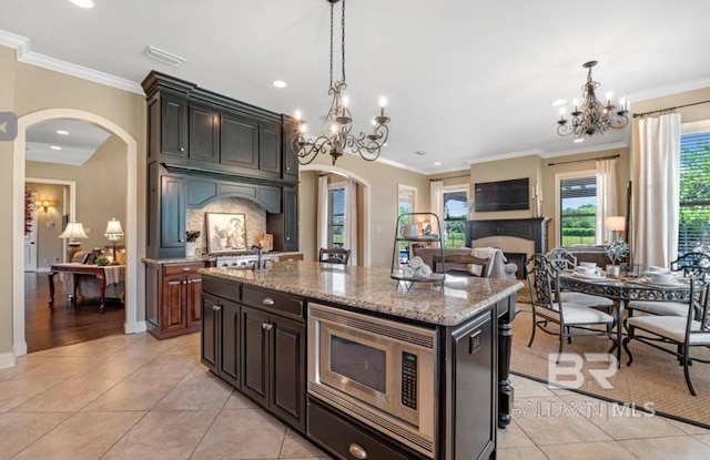 kitchen with ornamental molding, arched walkways, stainless steel microwave, and light tile patterned flooring