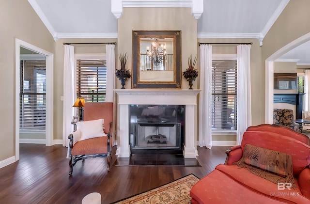 living area with baseboards, a fireplace with flush hearth, ornamental molding, wood finished floors, and a notable chandelier