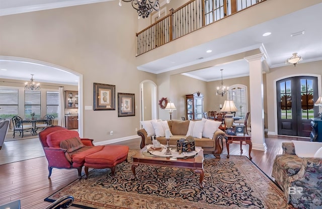 living area featuring a towering ceiling, ornamental molding, wood finished floors, a chandelier, and baseboards