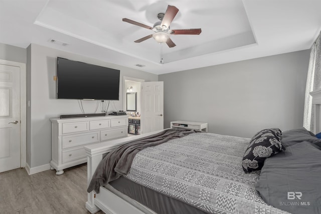 bedroom featuring light hardwood / wood-style flooring, ceiling fan, and a tray ceiling