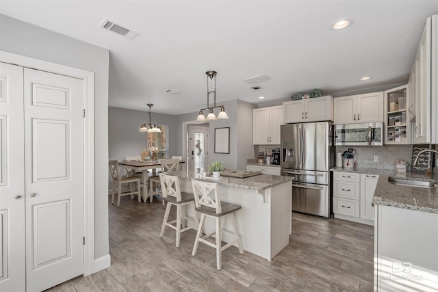 kitchen featuring sink, white cabinetry, light stone counters, a center island, and appliances with stainless steel finishes