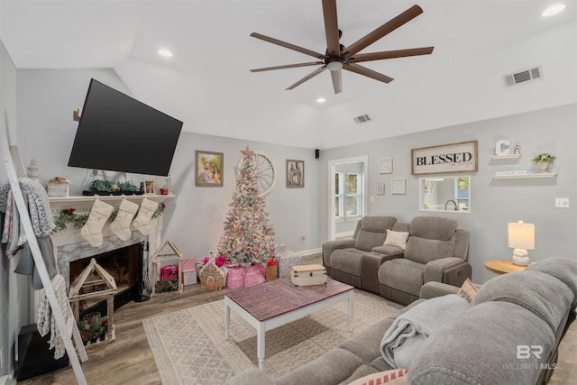 living room featuring light hardwood / wood-style flooring, a fireplace, ceiling fan, and vaulted ceiling