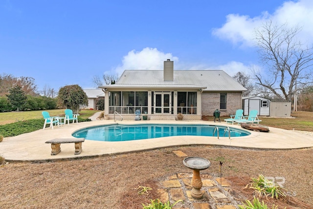 view of swimming pool with a sunroom, a patio area, and a storage shed