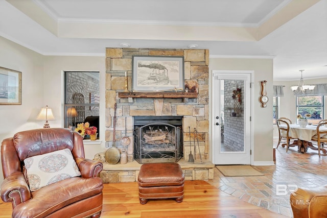 living room with crown molding, a tray ceiling, wood-type flooring, and a stone fireplace