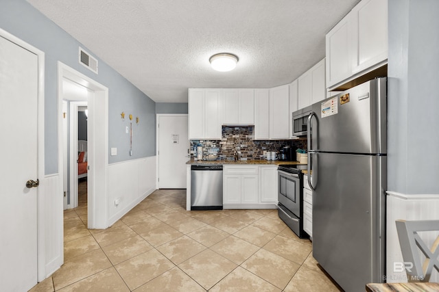 kitchen with backsplash, white cabinets, light tile patterned flooring, and appliances with stainless steel finishes