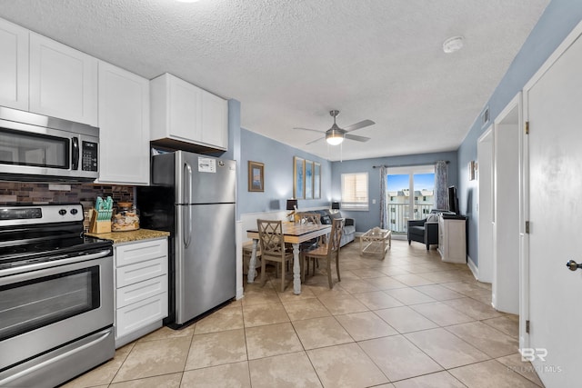 kitchen featuring ceiling fan, light tile patterned floors, backsplash, white cabinets, and appliances with stainless steel finishes