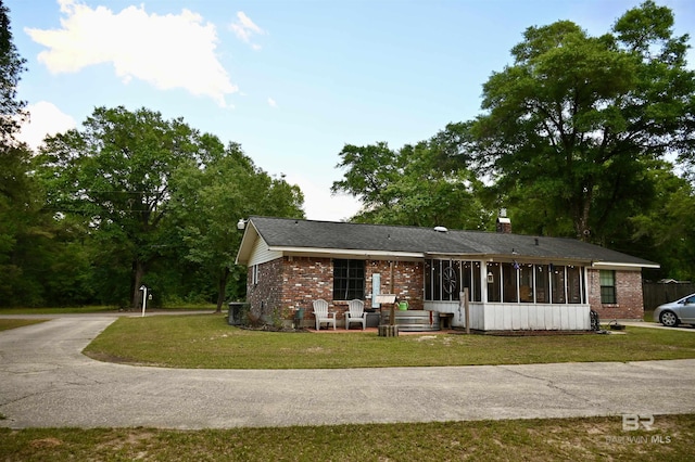 ranch-style house with brick siding, a front yard, a sunroom, and cooling unit