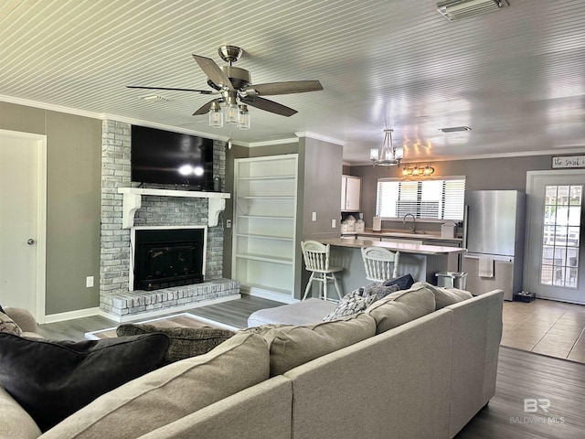 living area with crown molding, a fireplace, ceiling fan with notable chandelier, wood finished floors, and visible vents