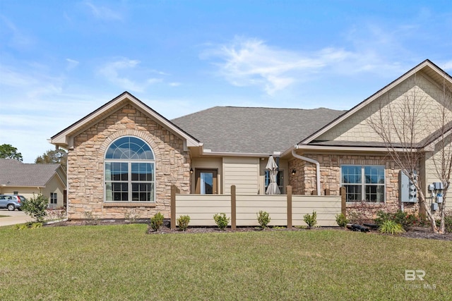 view of front of house with stone siding, a shingled roof, and a front lawn